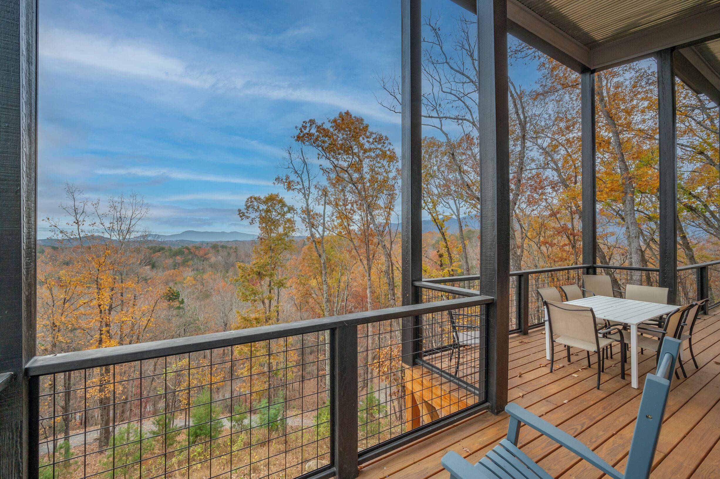 A wooden deck with a table and chairs, overlooking a forest with autumn foliage.