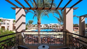 A balcony with two chairs and a table, overlooking a pool area with umbrellas and palm trees. - Magic World Sharm - Club By Jaz (Sharm El Sheikh)