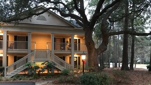 A two-story building with a balcony, a staircase, and a large tree in front. - Charming 2-bedroom condo in delightful Pawleys Island with AC, WiFi.   (Pawleys Island)