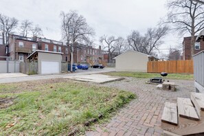 Un jardin à l’arrière d’une maison, avec une terrasse en briques, une clôture en bois et un garage.