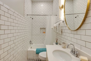 Une salle de bain avec des carreaux de céramique blancs rectangulaires, une baignoire blanche, un lavabo blanc et un miroir avec un cadre doré.
