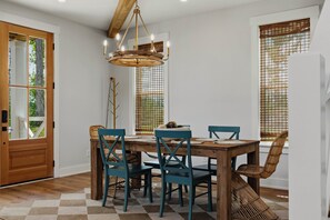 Uma sala de jantar com mesa de madeira, cadeiras verde-água, luminária pendente e janela com persiana de bambu.