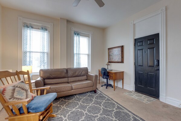A living room with a brown leather sofa, a wooden rocking chair, a desk with a chair, and a black door. - Quiet St Louis Apt: 3 Mi to Carondelet Park (St. Louis)