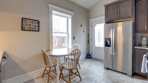 Une cuisine équipée d’un grand réfrigérateur, d’une table à manger avec des chaises et d’une fenêtre donnant sur des immeubles.