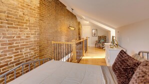 Une chambre avec un mur en briques, un plancher en bois, un lit, une commode et une chaise.