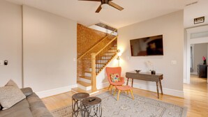 Un salon avec un escalier, un canapé, une table basse et un téléviseur fixé au mur.