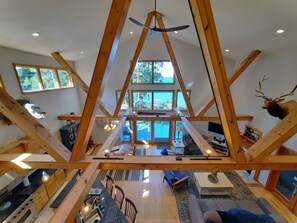 A spacious loft with high ceilings, exposed wooden beams, a large dining area, and a view of the outdoors.