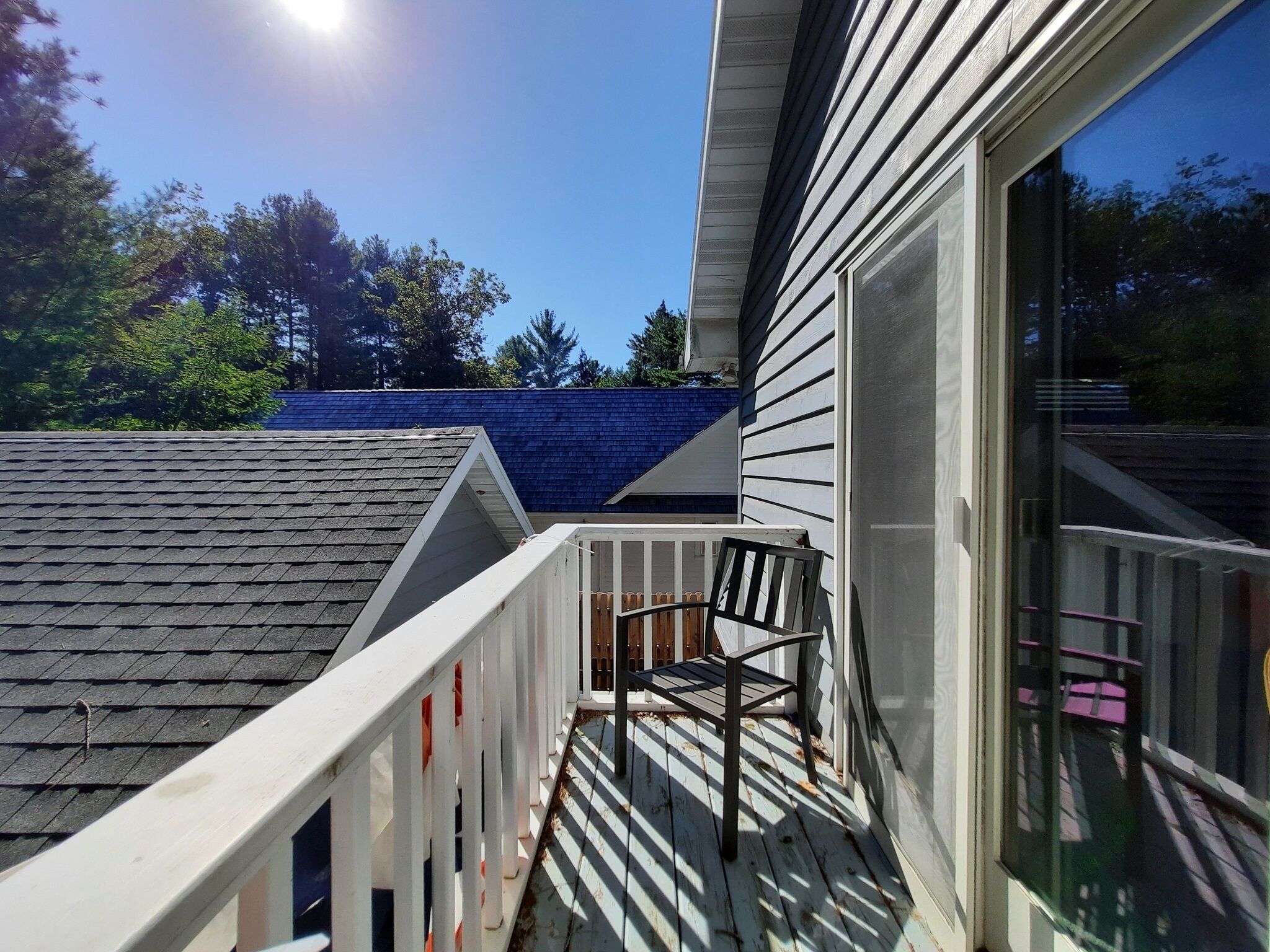 Une terrasse en bois avec une chaise, une porte vitrée et un toit bleu.