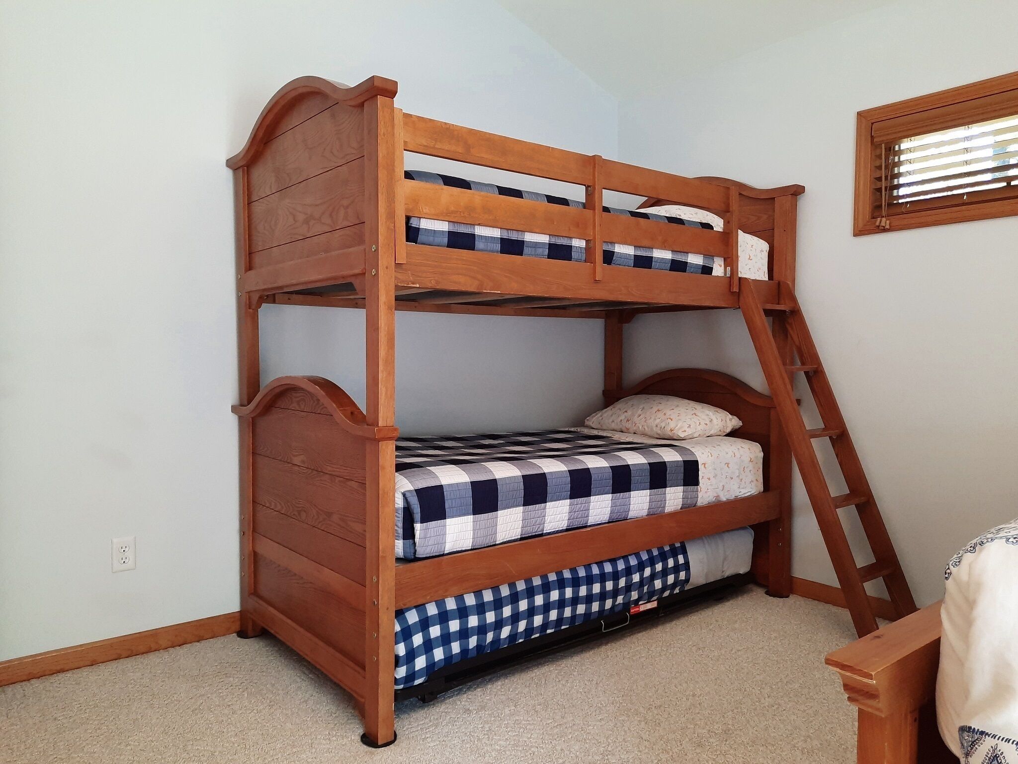 A bunk bed with a ladder, checkered bedding, and a window with blinds.
