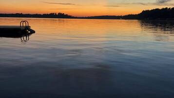 A calm lake at sunset with a dock and a row of trees in the background.