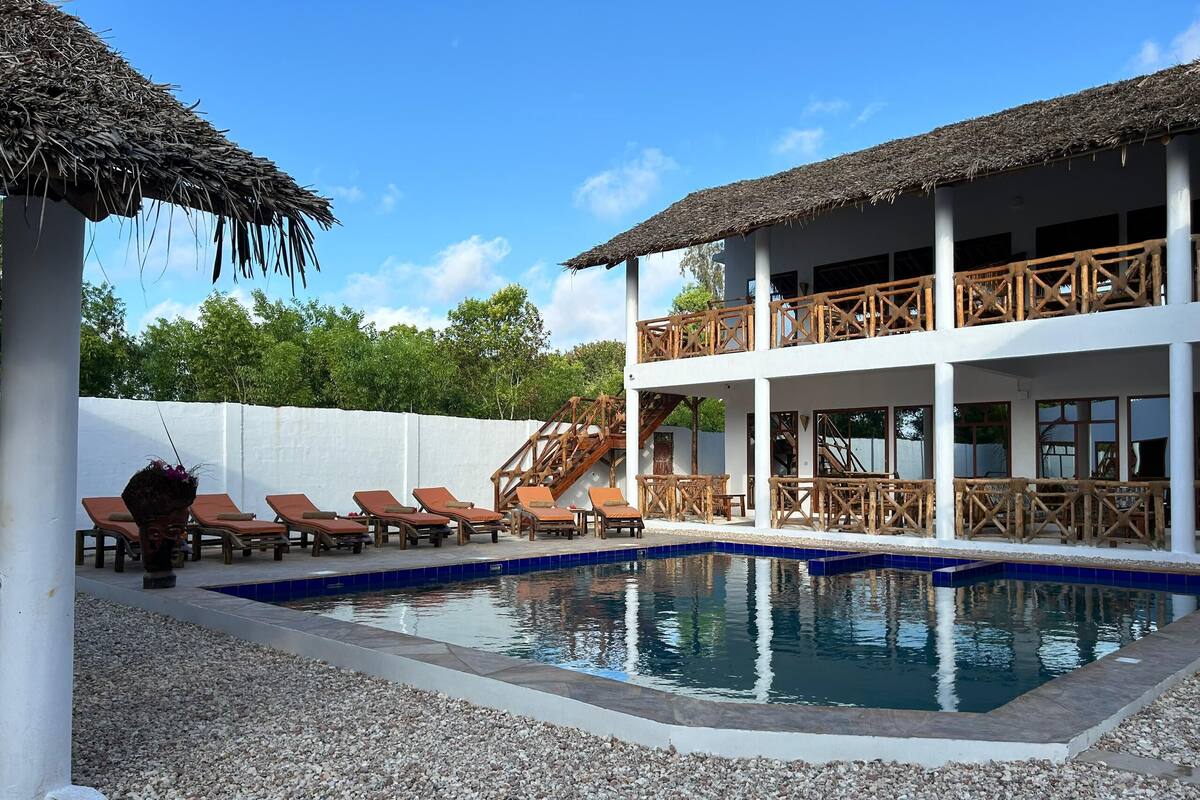 A pool area with lounge chairs, a staircase, and a building with wooden railings.