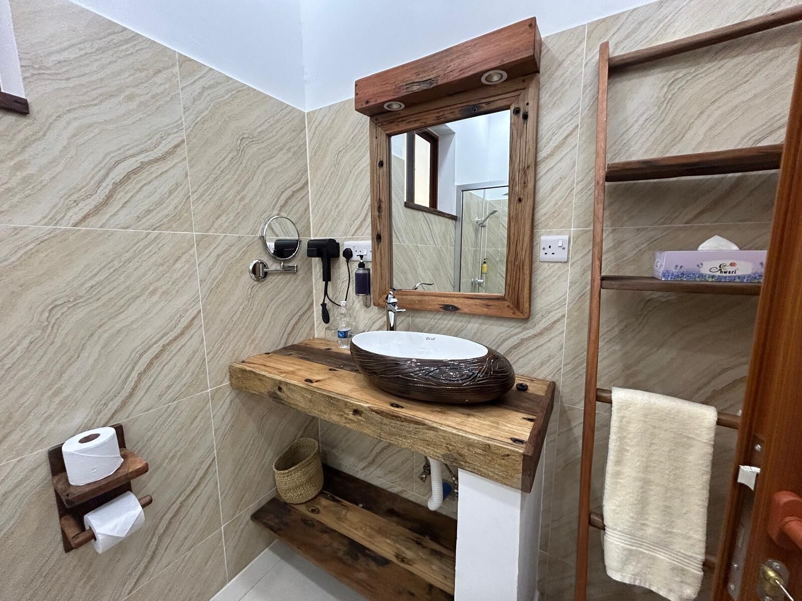A bathroom with a wooden vanity, a round sink, a mirror, and a towel rack.