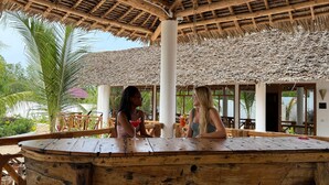 An outdoor seating area with a thatched roof, wooden tables, and chairs. - M&m Villas Zanzibar (Kidoti)