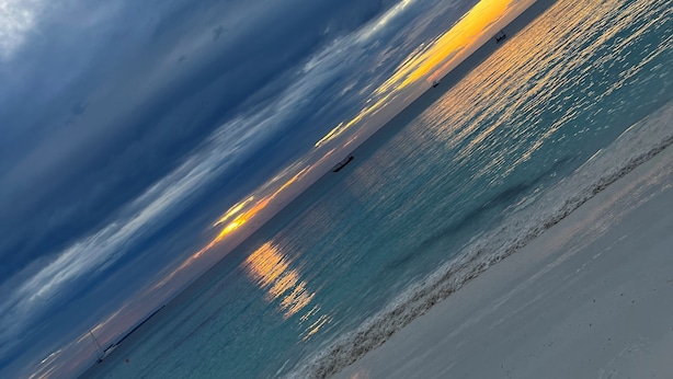 A beach with a sunset, calm water, and a distant boat. - M&m Villas Zanzibar (Kidoti)