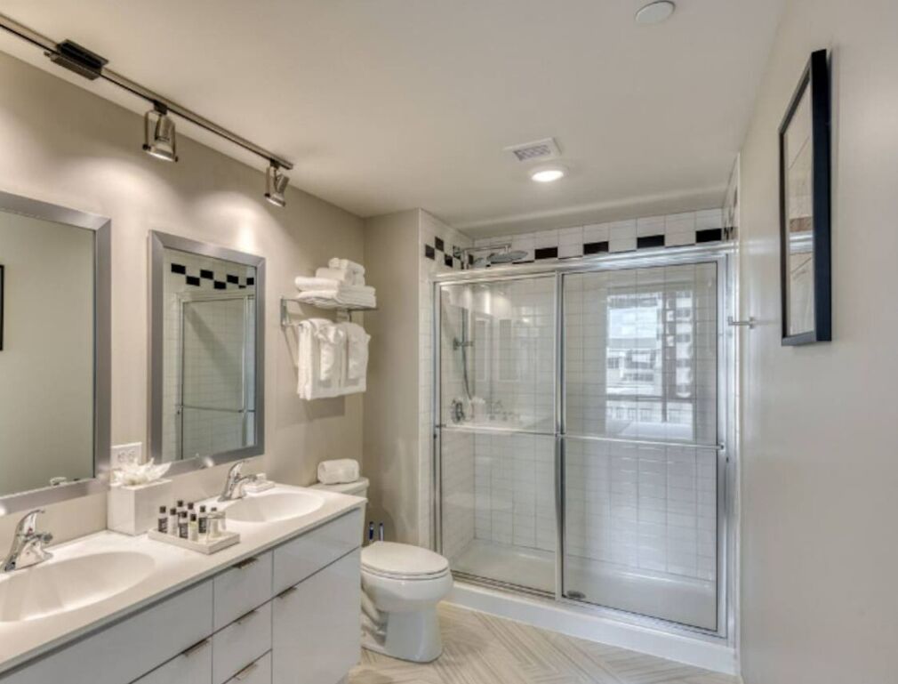 A modern bathroom with a large mirror, a double sink vanity, a toilet, and a glass-enclosed shower.