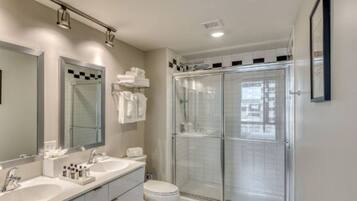 A modern bathroom with a large mirror, a double sink vanity, a toilet, and a glass-enclosed shower.