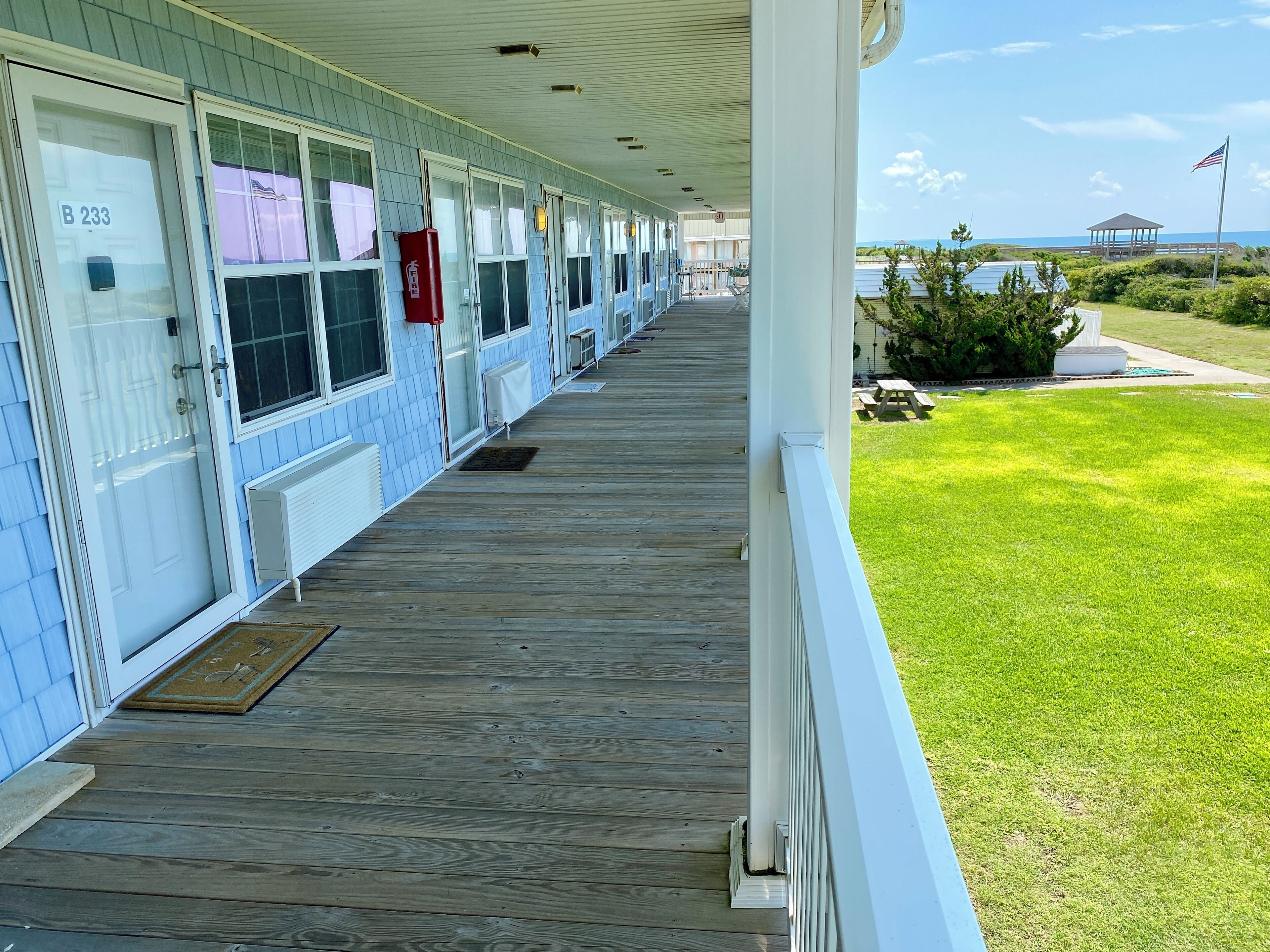 A hotel with a covered porch, multiple rooms with windows, and a view of the ocean.