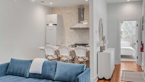 A modern living room with a blue sofa, a dining area with wicker chairs, and a kitchen with white cabinets and a stove. - The Philip's Suite, newly renovated 3 Bed/3 EnSuite Bath, 1 Block to King (Charleston)