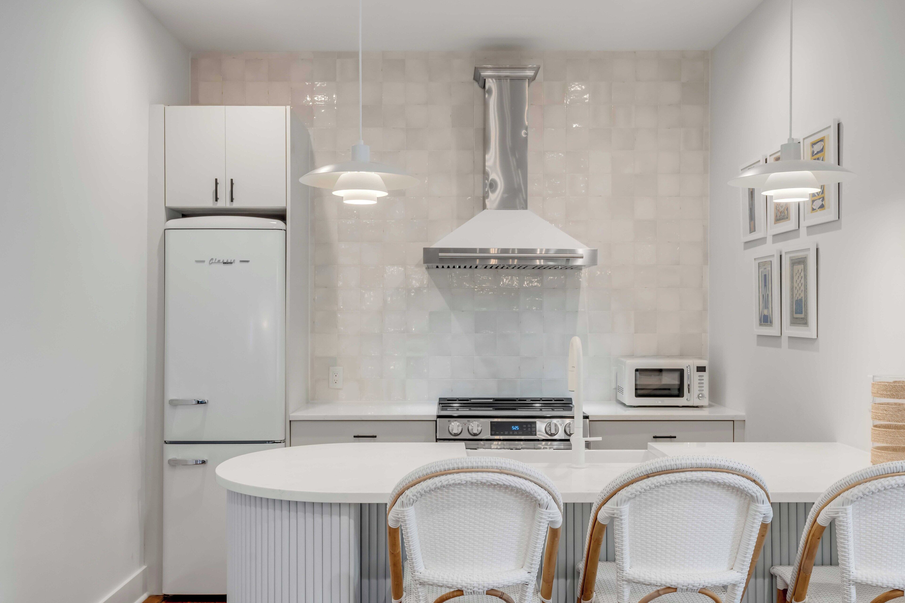 A modern kitchen with white cabinetry, a central island with chairs, a stove, and a microwave.
