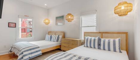 A bedroom with two beds, a wooden dresser, a ceiling fan, and a window with blinds.