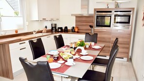 Eine moderne Küche mit Essbereich, ausgestattet mit Edelstahlgeräten, einer Kaffeemaschine und verschiedenen Küchenutensilien.