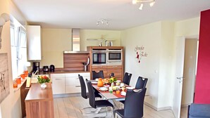 Eine moderne Küche mit integrierten Geräten, ein Essbereich mit Holztisch und schwarzen Stühlen sowie eine rote Akzentwand.