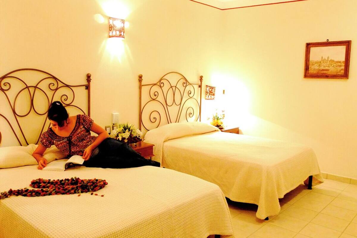 A hotel room with two single beds, a nightstand with a lamp, and a wall-mounted picture.