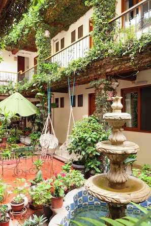 A courtyard with a fountain, potted plants, and outdoor seating. - Hotel Dainzú (Oaxaca)