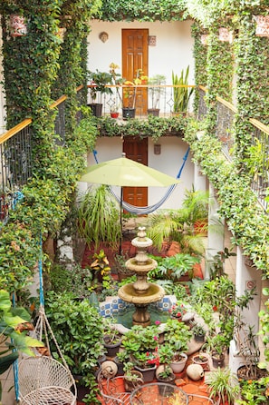 A courtyard with a central fountain, surrounded by potted plants and a hammock. - Hotel Dainzú (Oaxaca)