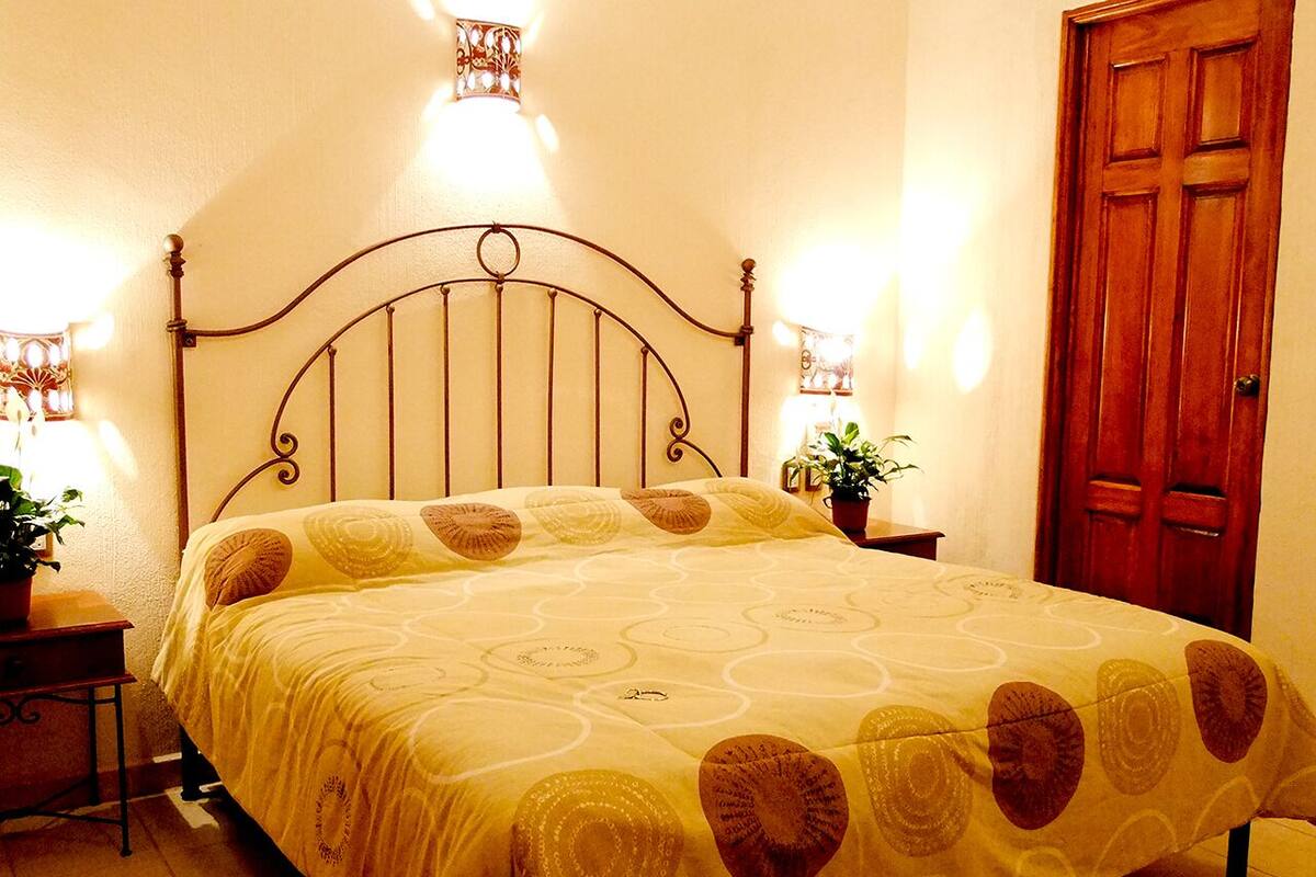 A neatly made bed with a patterned bedspread, a wooden headboard, and two bedside tables with lamps.