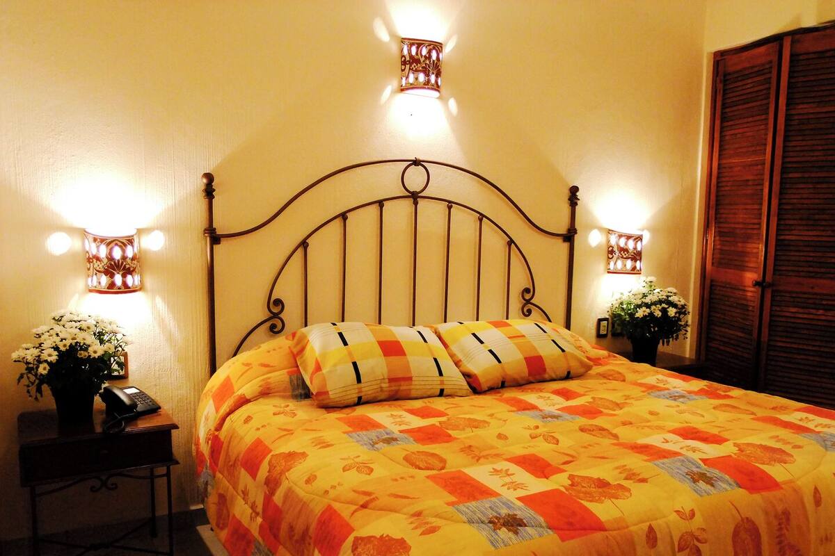 A bed with a metal headboard, two bedside lamps, a nightstand with a phone, and a potted plant.