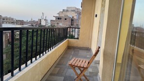 A balcony with a wooden chair, a black metal railing, and a view of buildings in the background. - Pyramids Hotel (Giza)