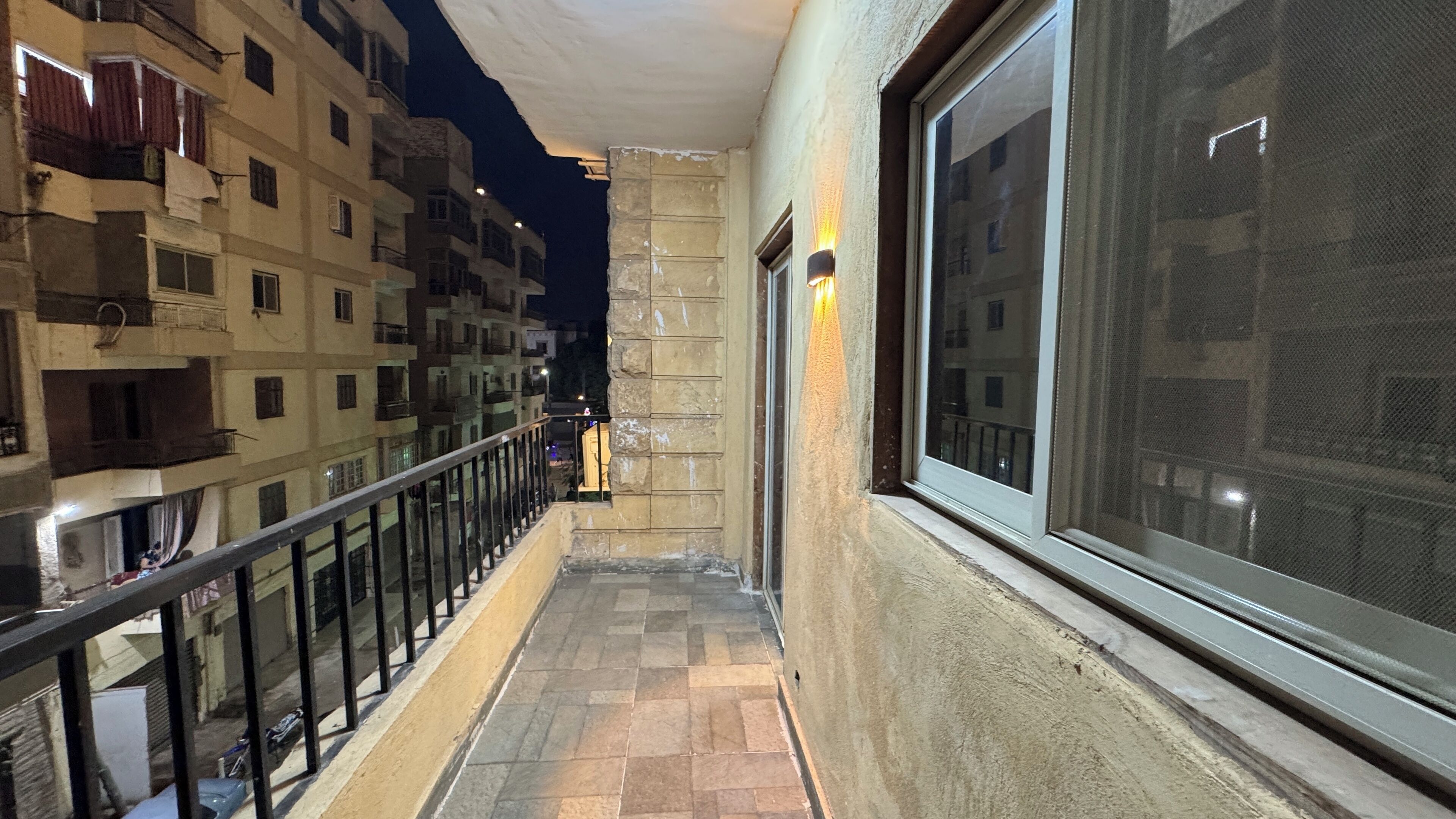 A narrow balcony with a tiled floor, a metal railing, and a large window on the right.