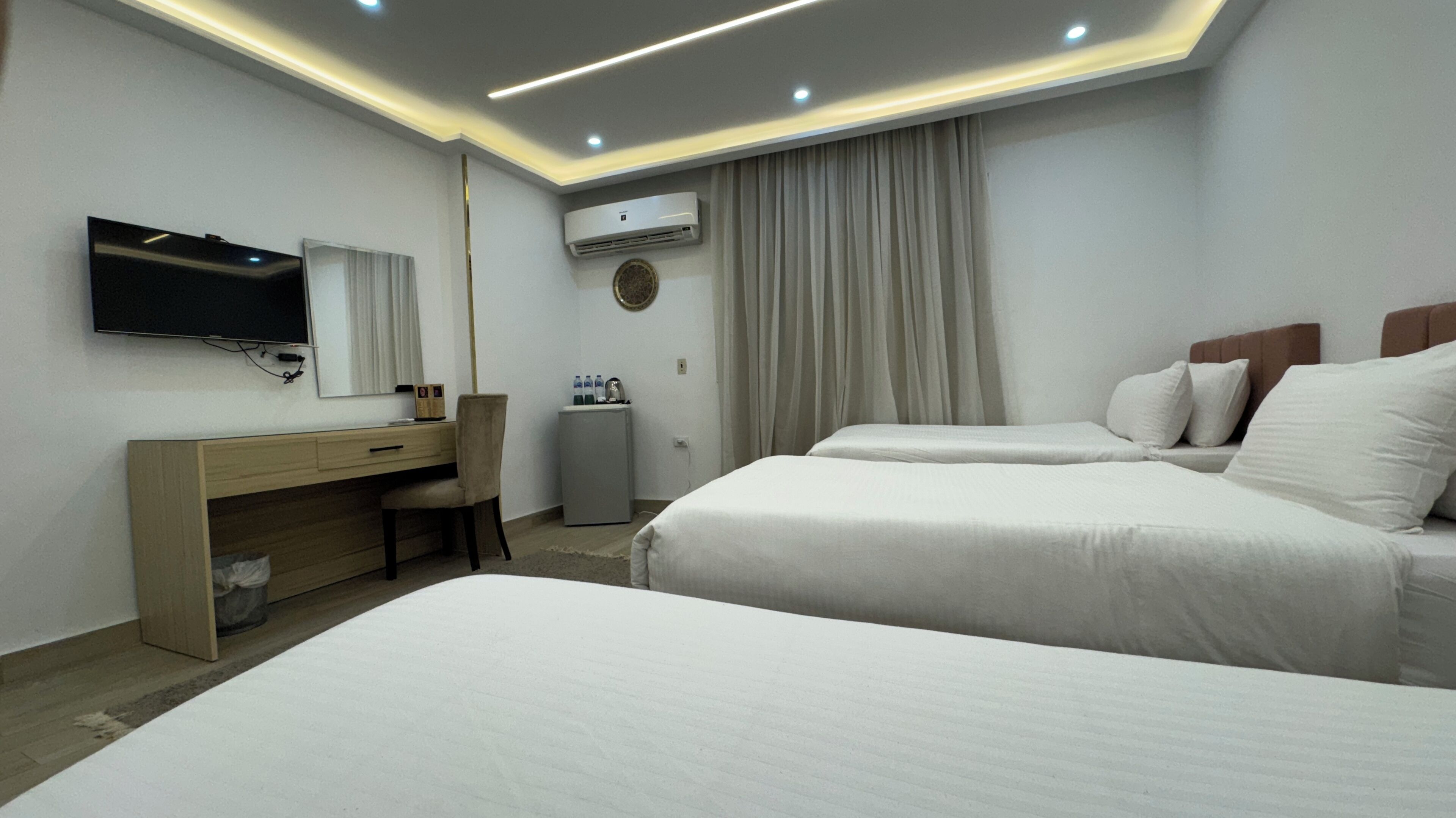 A hotel room with two beds, a desk, a TV, an air conditioner, and a minibar.