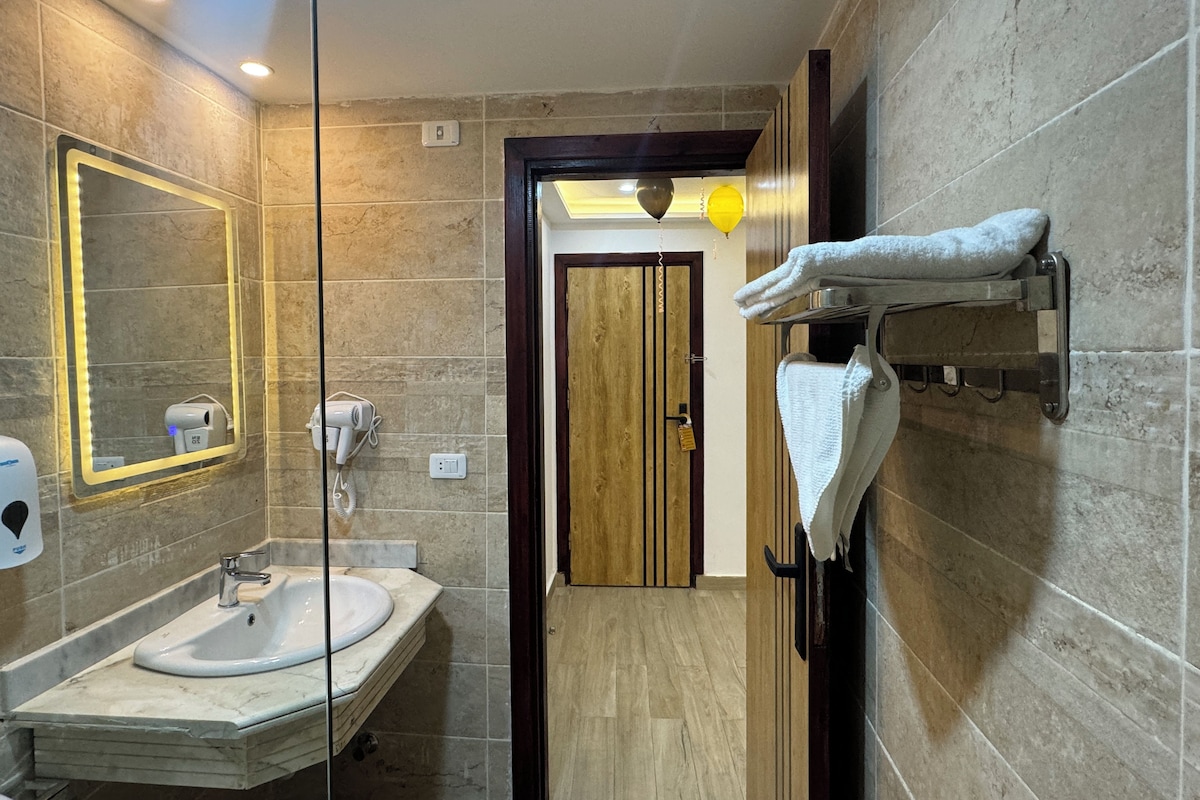 A modern bathroom with a marble sink, a glass-enclosed mirror, a hairdryer, and a towel rack.