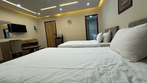 Ein Hotelzimmer mit zwei Betten, einem Schreibtisch, einem Fernseher und einem durch eine Glastür einsehbaren Badezimmer.