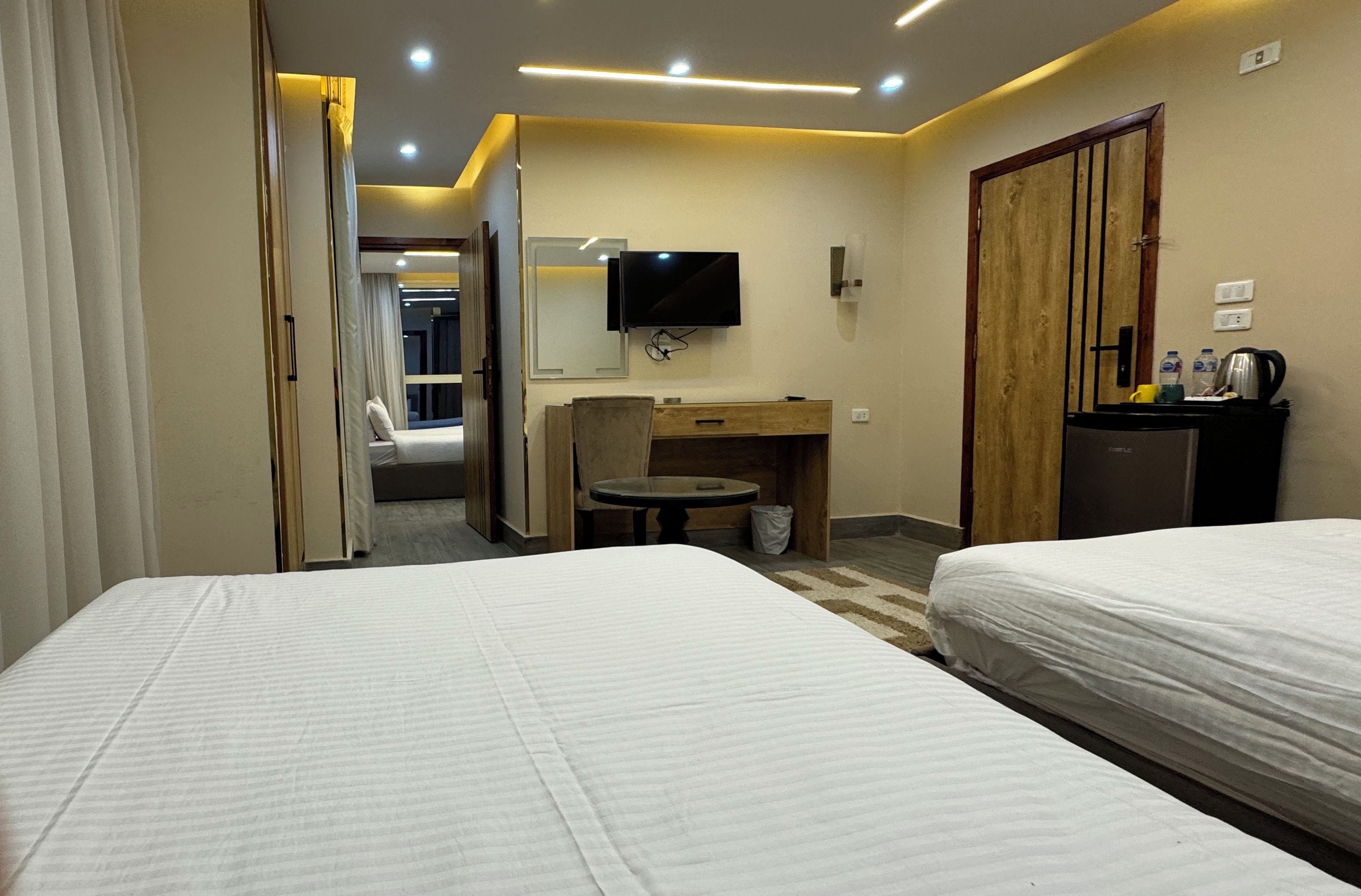 A hotel room with two beds, a TV, a wooden cabinet, a small round table, and a door leading to another room.