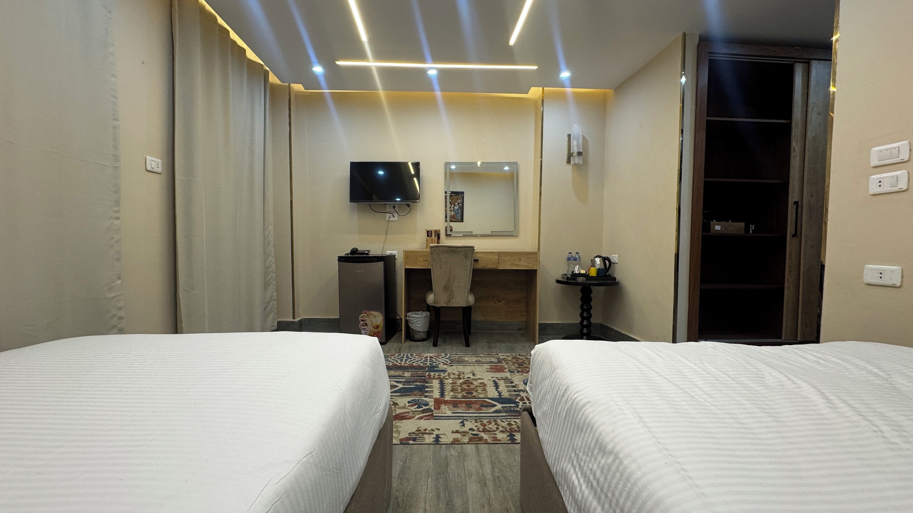 A hotel room with two beds, a desk, a chair, a TV, and a small table with toiletries.