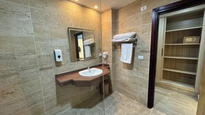 A bathroom with a marble-tiled wall, a sink with a vanity, a mirror, a towel rack, and a wooden cabinet. - Pyramids Hotel (Giza)