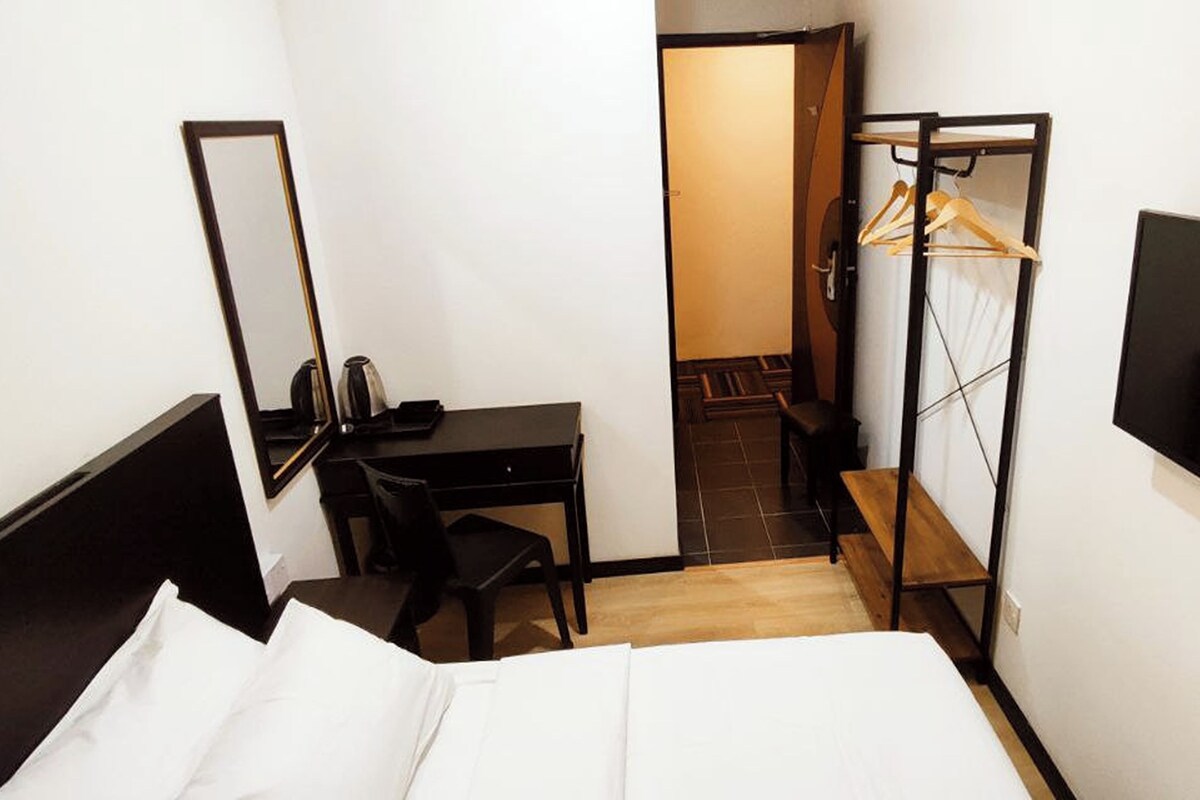 A hotel room with a bed, a desk, a chair, a TV, and a wardrobe with a mirror.