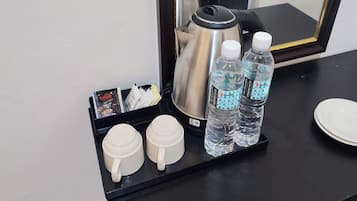 A coffee station with two white cups, two water bottles, a coffee pot, and a tray with magazines and a small box.