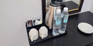 A coffee station with two white cups, two water bottles, a coffee pot, and a tray with magazines and a small box.