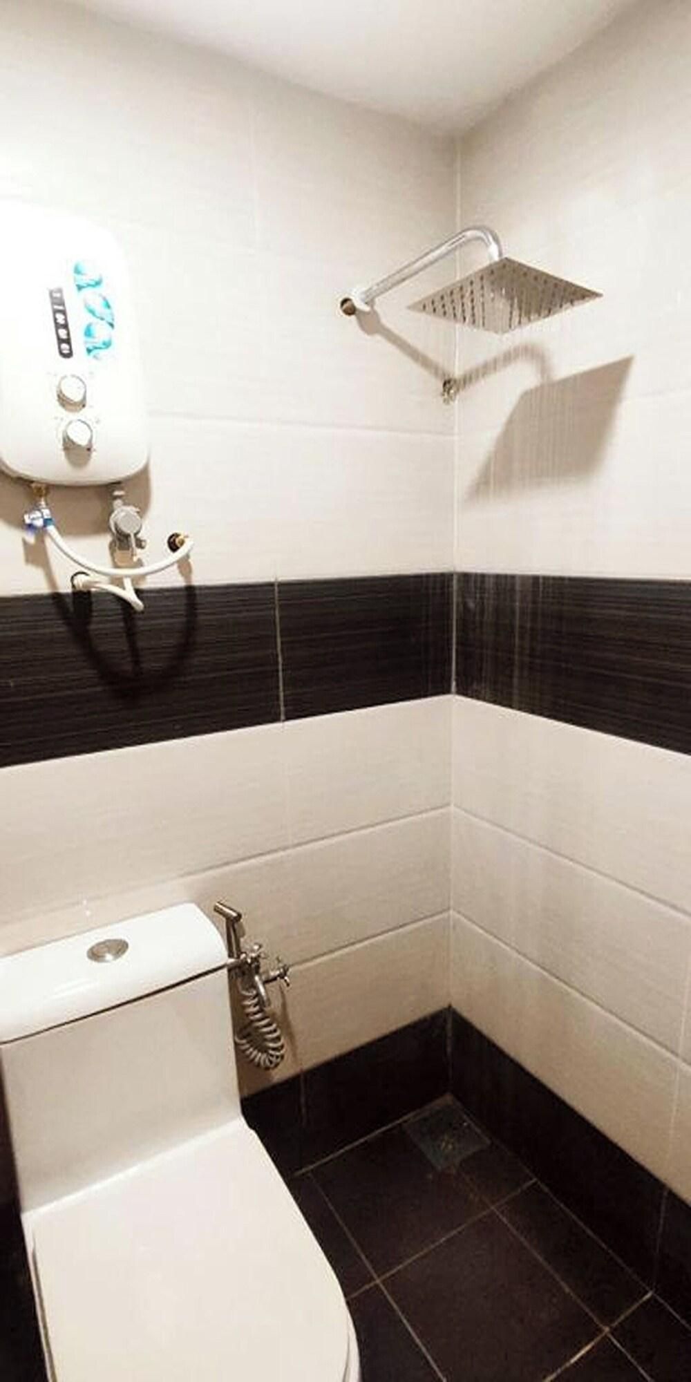 Baño en esquina con inodoro, ducha y secamanos fijado a la pared.