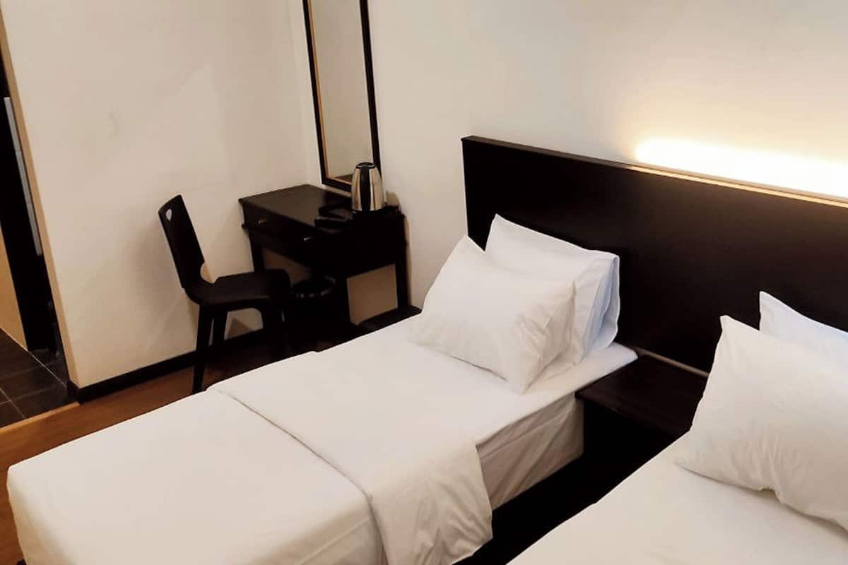 Quarto de hotel com duas camas de solteiro, uma escrivaninha e uma cadeira.