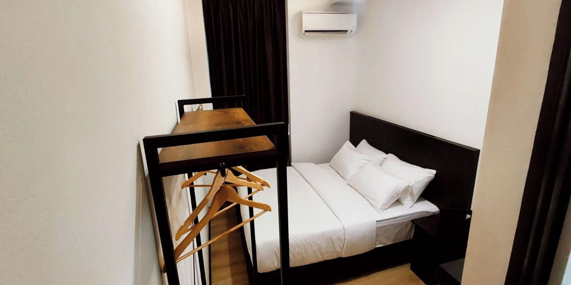 Una habitación pequeña con cama, una mesita y un perchero de madera.