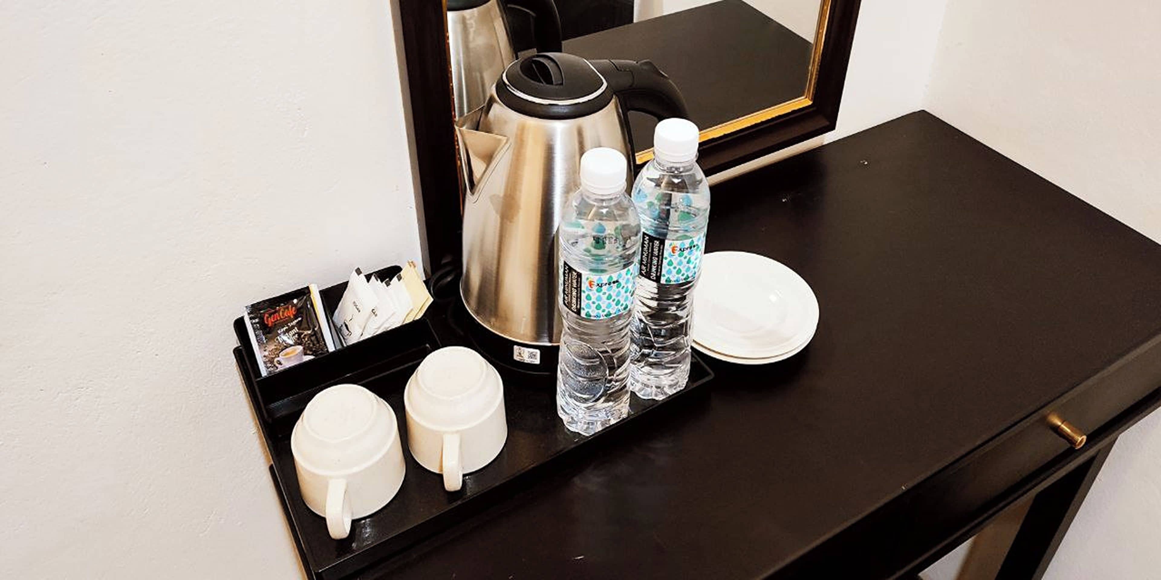 A tray with two white mugs, two water bottles, a coffee pot, and a plate on a black table.
