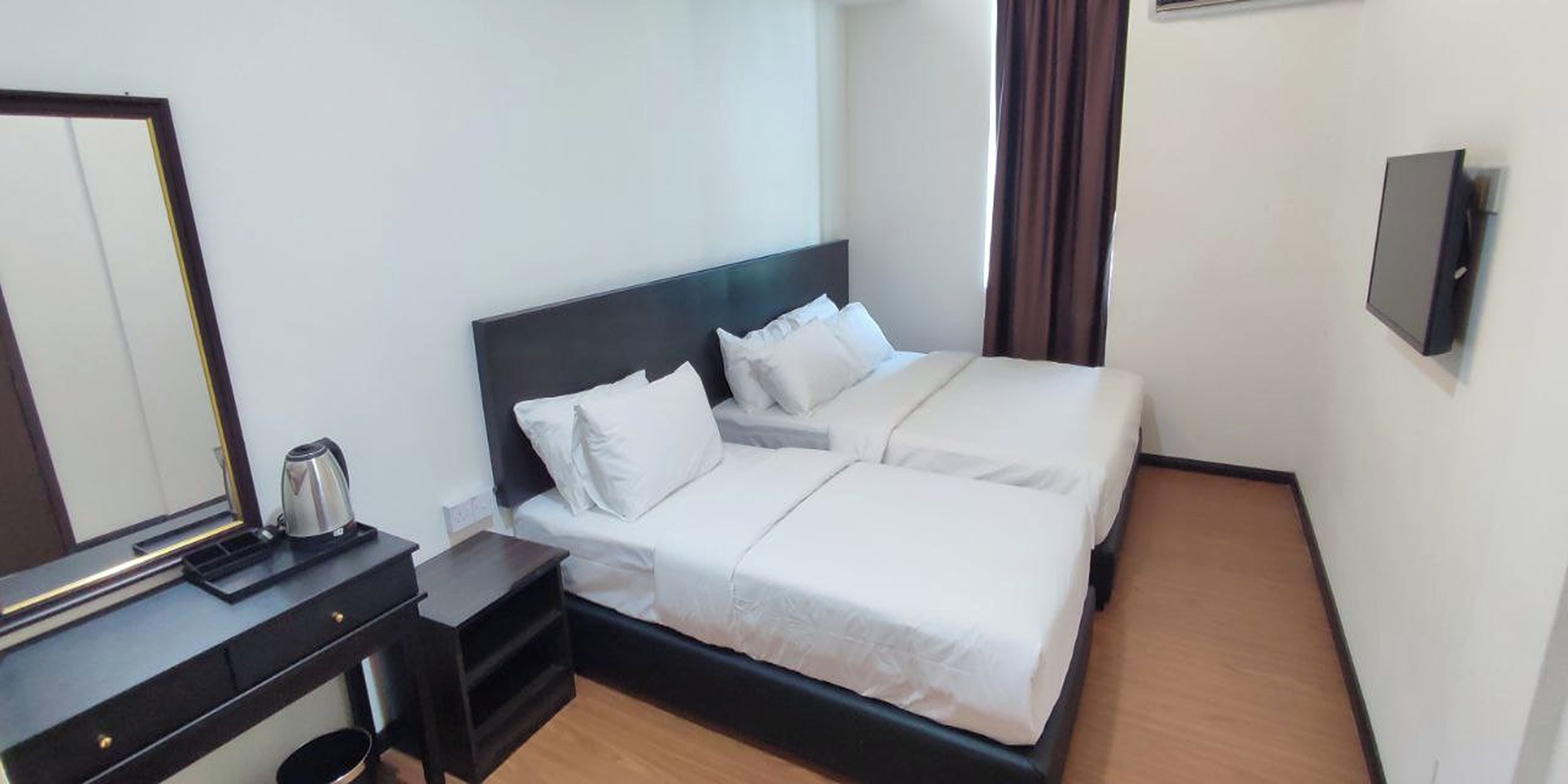 A hotel room with a double bed, a bedside table with a kettle, a mirror, and a wall-mounted TV.