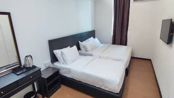 A hotel room with a double bed, a bedside table with a kettle, a mirror, and a wall-mounted TV.