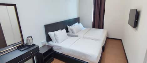 A hotel room with a double bed, a bedside table with a kettle, a mirror, and a wall-mounted TV.