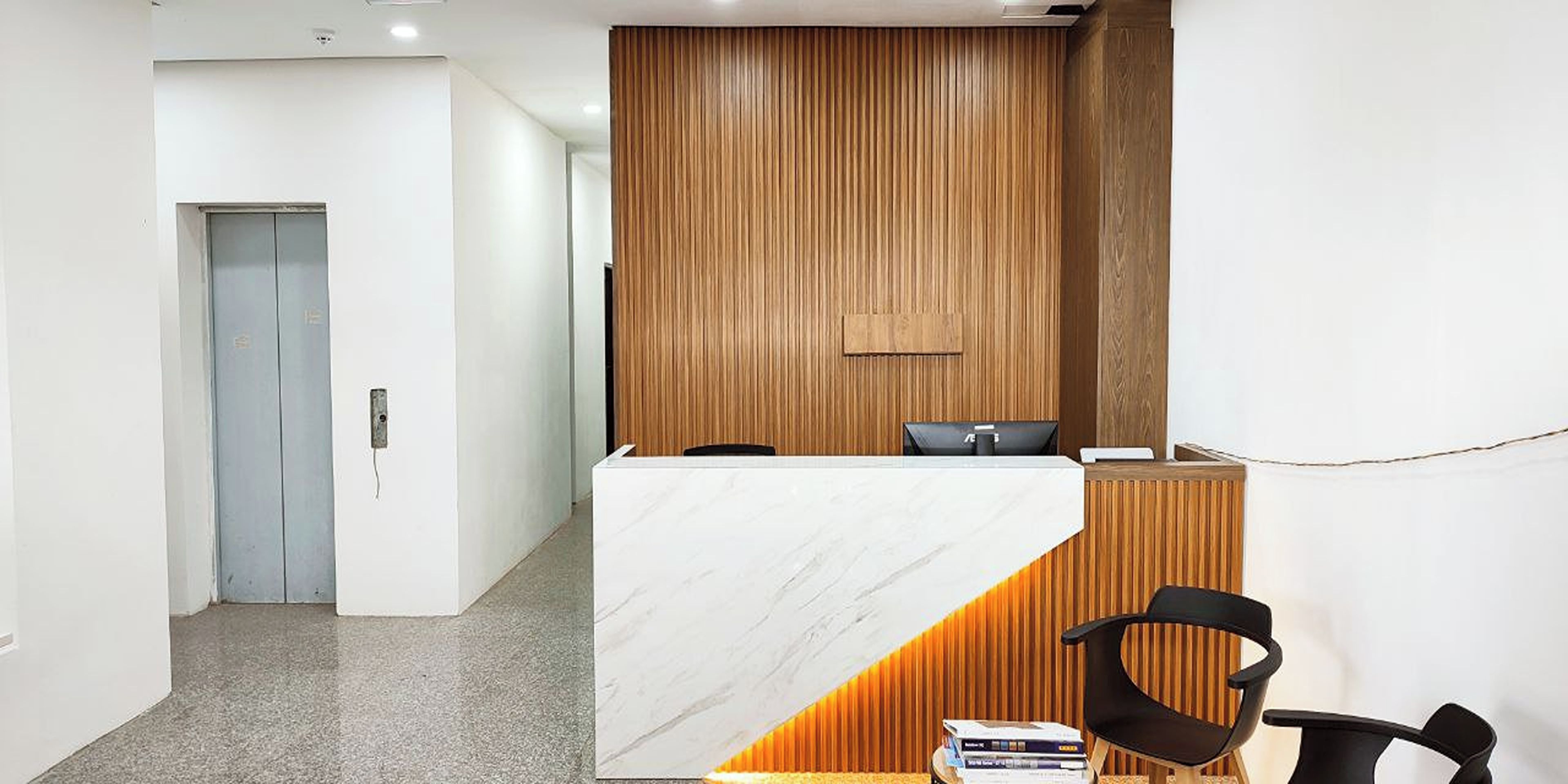 Zona de recepción con mostrador de mármol, panel de pared de madera y sillas negras.